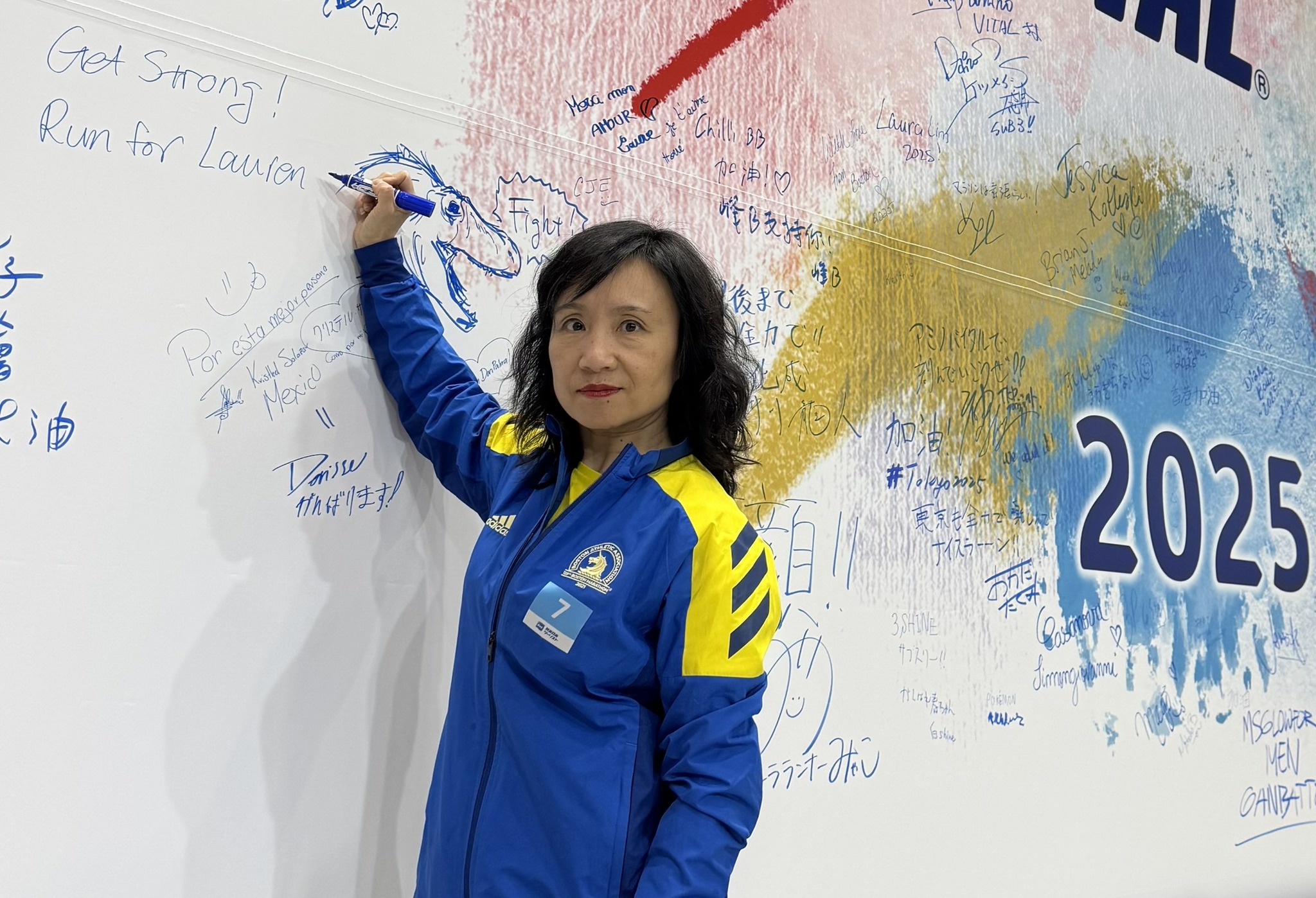 Dr. Holly Wang participating in 2025 Tokyo Marathon, and running for Lauren. Writing on large wall "Run for Lauren"